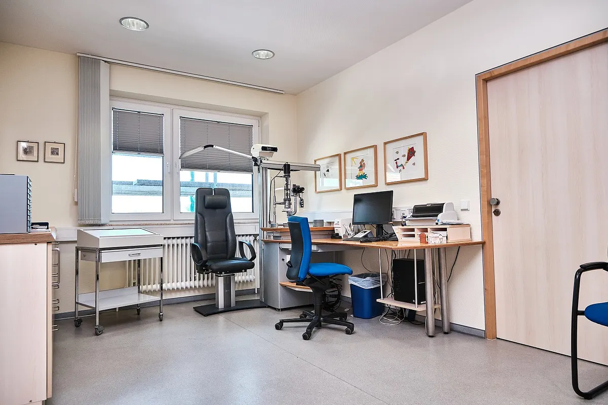 Untersuchungszimmer mit Schreibtisch, Bildschirm und Untersuchungsgeräten